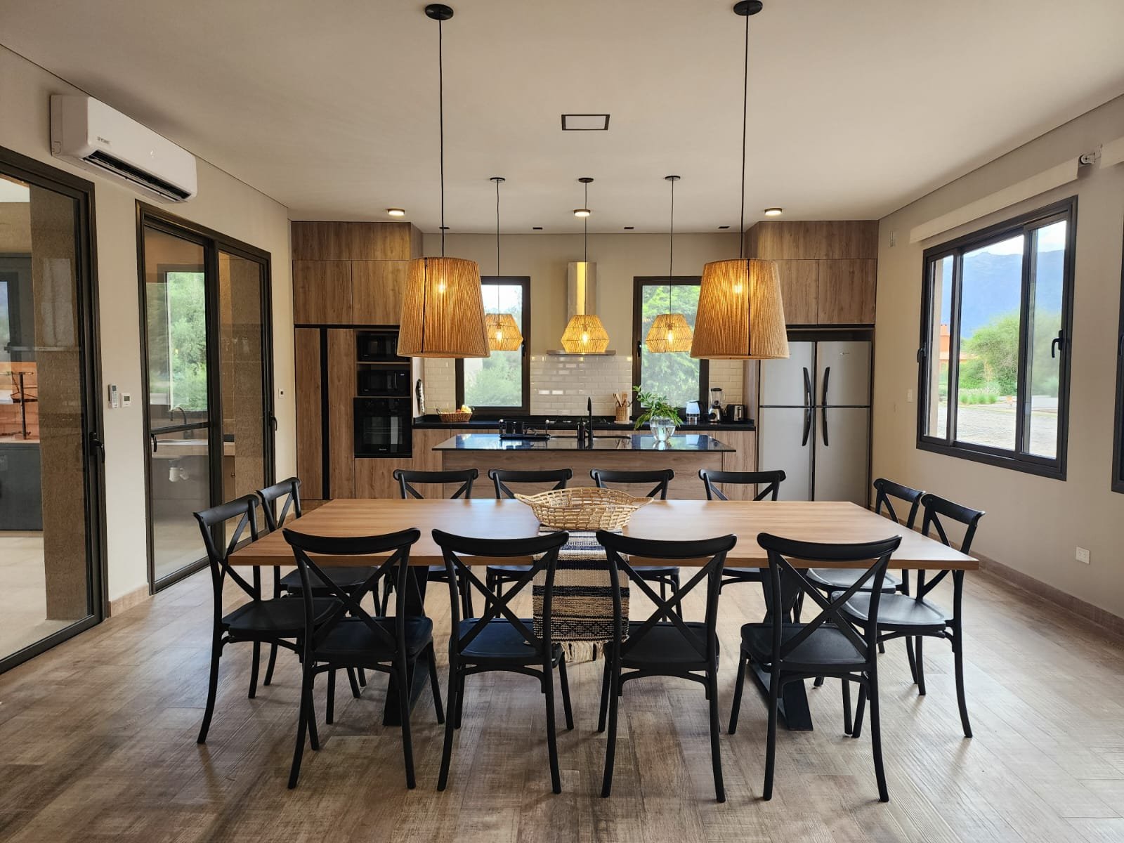 Comedor y cocina integrados, estilo rústico moderno, mesa madera, lámparas colgantes — proyecto Ca La Estancia, por Luciana González Anderson, en Cafayate